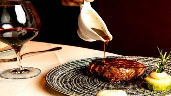 sauce poured onto steak with red wine glass from Reserve Cut NYC